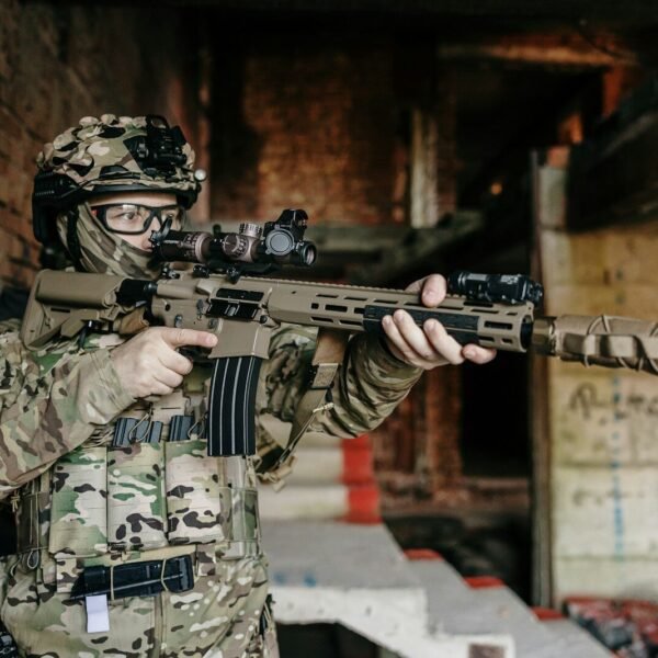 Soldier in camouflage holding a rifle indoors.
